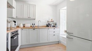 Una cocina con gabinetes blancos, encimera de madera, horno empotrado, refrigerador y un lavamanos.