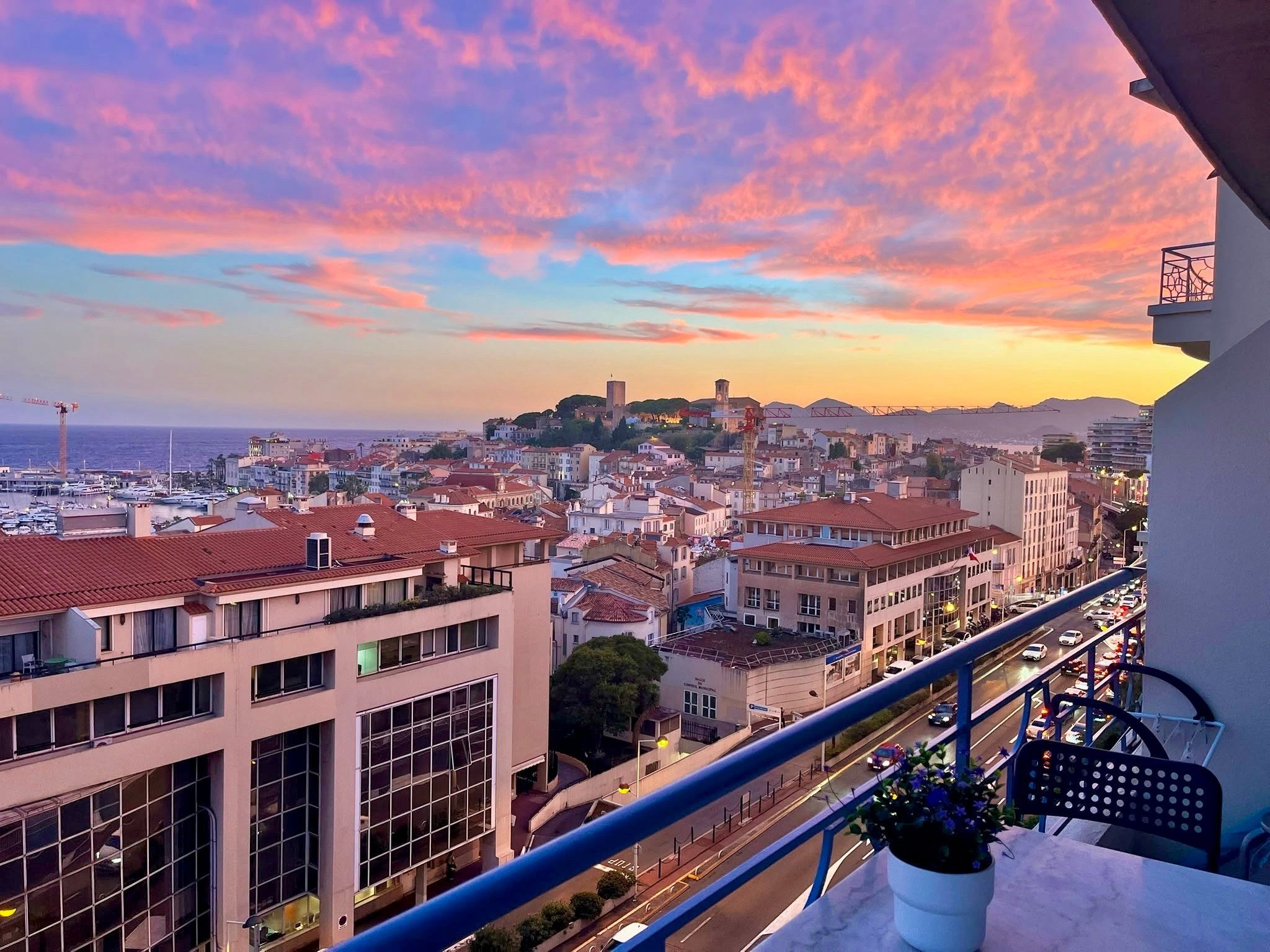 A balcony with a city view at sunset, featuring buildings, a bridge, and a distant hill.