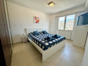 A bedroom with a bed, a window, and a view of buildings outside. - Charmant 3P vue mer balcon panoramique, Clim (Cannes)