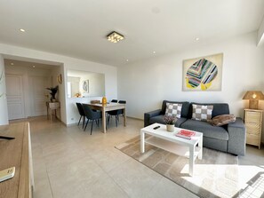 A modern living room with a grey sofa, a white coffee table, and a dining area with a wooden table and chairs. - Charmant 3P vue mer balcon panoramique, Clim (Cannes)