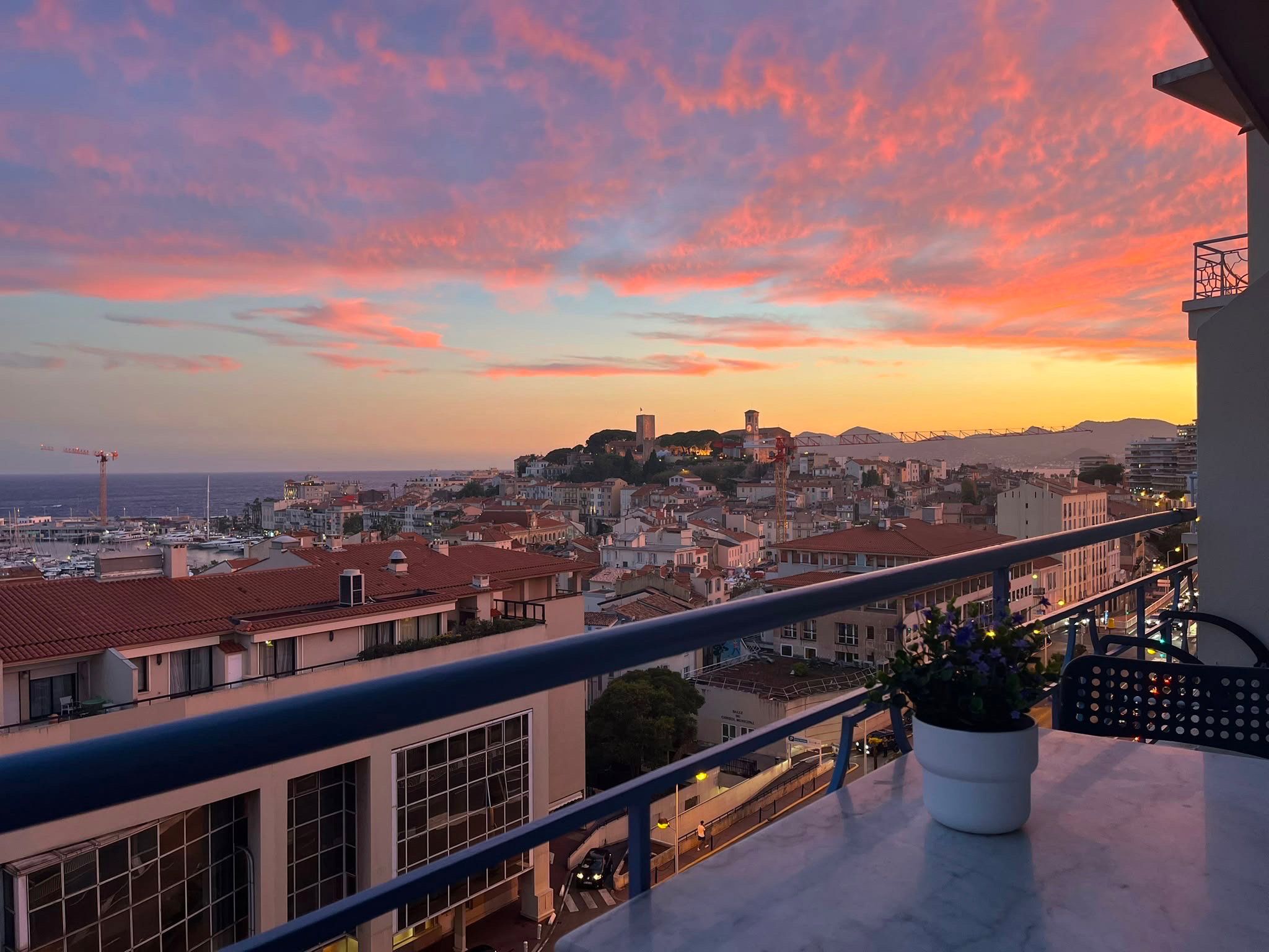 A balcony with a view of a cityscape at sunset, including buildings and a distant tower.