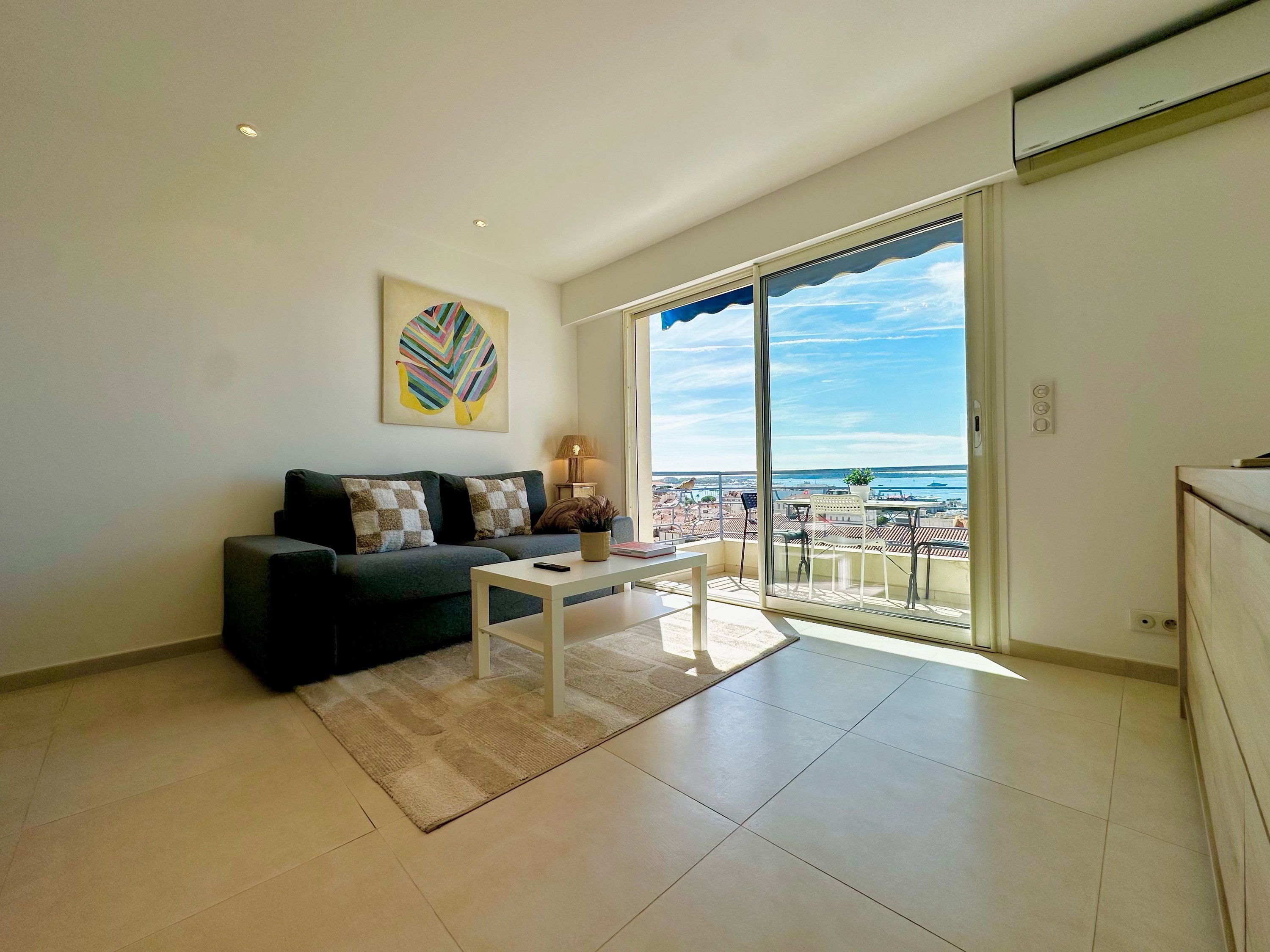 A modern living room with a sofa, a coffee table, and a view of the sea through large glass doors.
