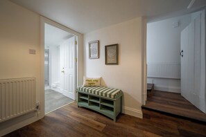 A hallway with a bench, a radiator, and a door leading to another room. - The Cottage at Old Coombe House (Tetbury)