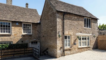 A stone cottage with a traditional design, featuring a gravel driveway and a wooden gate.