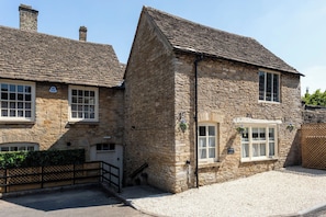 A stone cottage with a traditional design, featuring a gravel driveway and a wooden gate. - The Cottage at Old Coombe House (Tetbury)