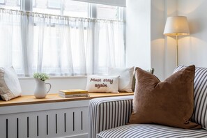 A room with a window, a radiator, a lamp, a striped sofa, and a cushion with a motivational quote. - The Cottage at Old Coombe House (Tetbury)