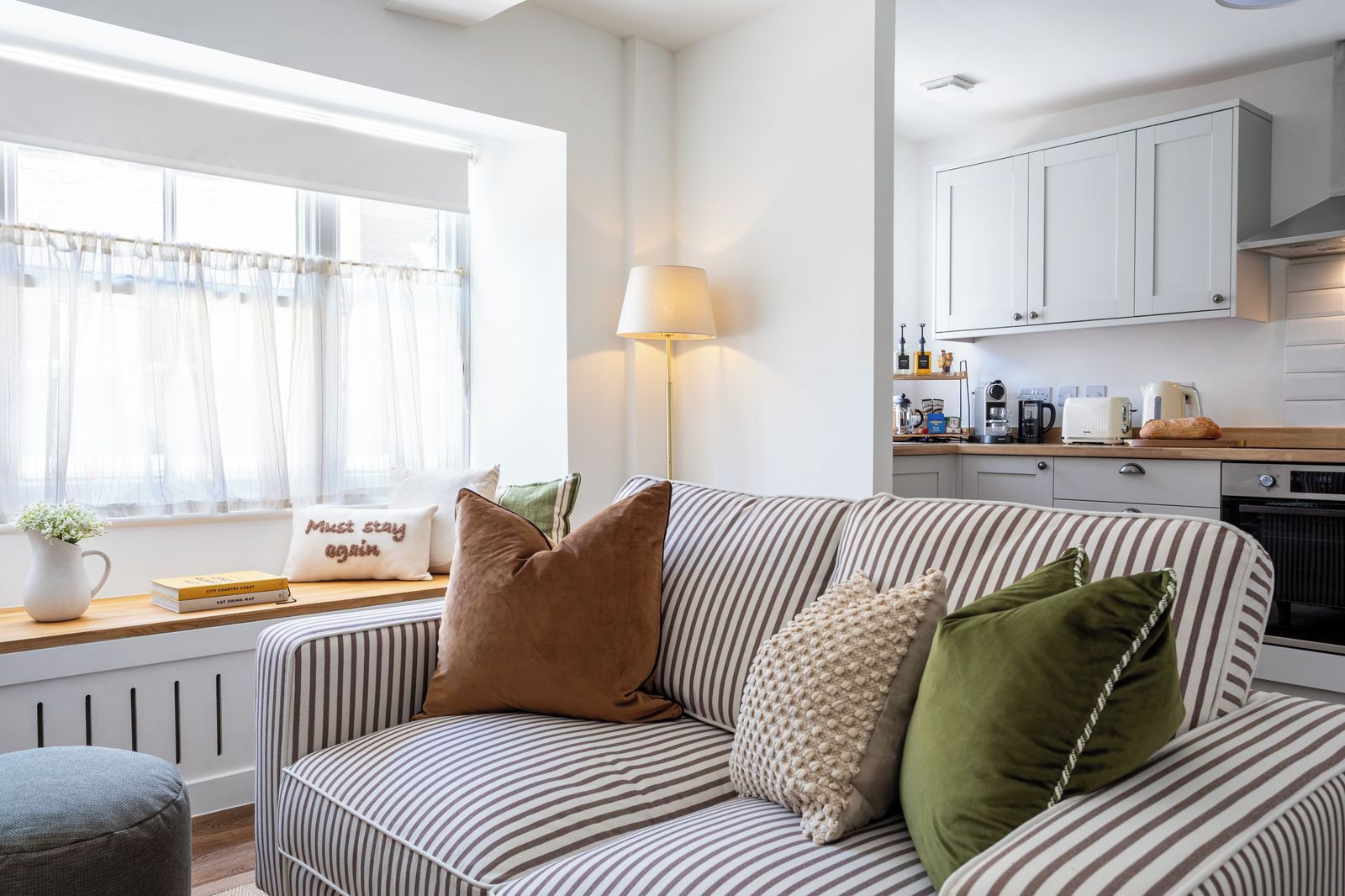A cozy living room with a striped sofa, a lamp, and a window with sheer curtains.