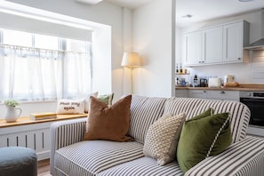 A cozy living room with a striped sofa, a lamp, and a window with sheer curtains. - The Cottage at Old Coombe House (Tetbury)