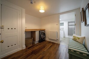 A laundry room with a washing machine, a radiator, and a wooden counter. - The Cottage at Old Coombe House (Tetbury)