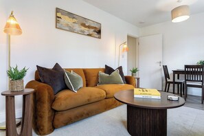 A modern living room with a brown sofa, two side tables, a coffee table, and a painting on the wall. - New! Stylish King Bed Apartment | Central Lechlade (Lechlade)