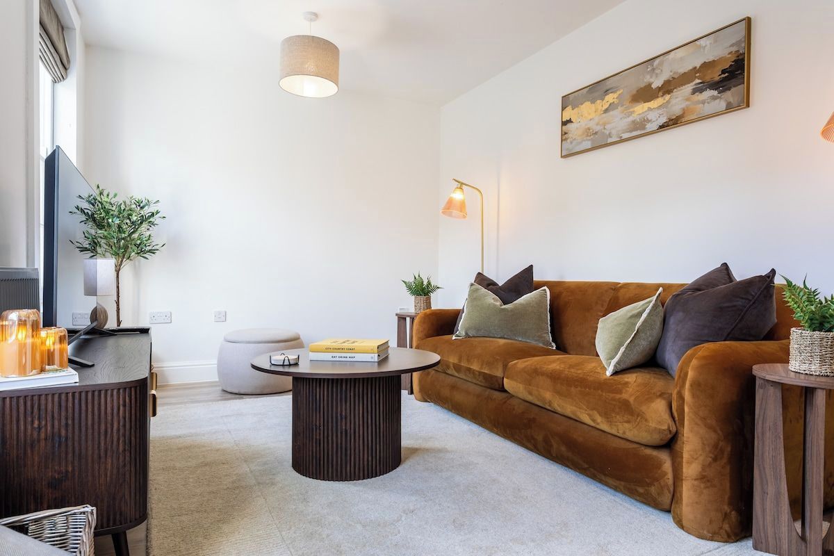 Ein modernes Wohnzimmer mit einem braunen Sofa, einem runden Couchtisch und einem Flachbildfernseher.