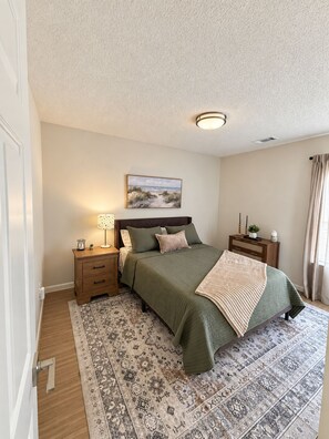 A bedroom with a bed, nightstands, a lamp, a painting, and a patterned rug.