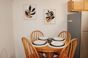Un coin repas avec une table en bois, six chaises et deux œuvres d’art représentant des feuilles, encadrées et accrochées au mur.
