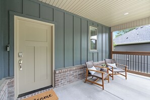 A front porch with a door, two wicker chairs, a brick wall, and a window. - Trailfront Ride & Reel - Upscale Retreat 4bd/2.5ba Sleeps 10 - HOT TUB! (Bella Vista)