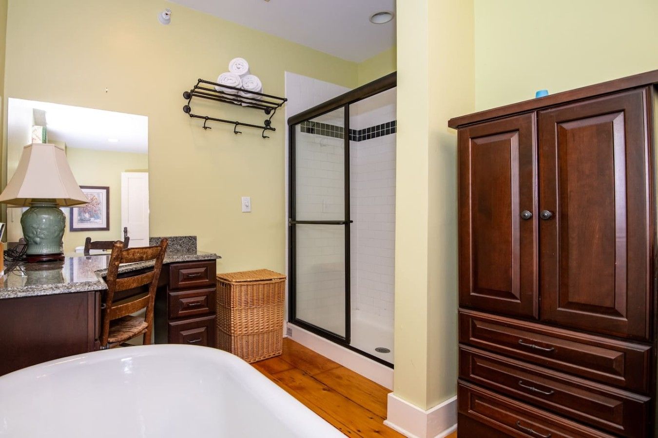 A bathroom with a bathtub, wooden cabinets, a wicker basket, and a towel rack.