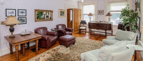 A living room with a wooden coffee table, leather armchairs, a patterned rug, a sofa, a piano, and framed artwork on the walls.