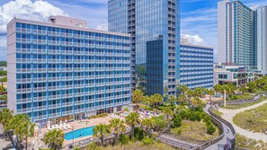 A hotel with multiple floors, a swimming pool, and a landscaped area with palm trees. - Oceanfront Serenity at Yachtsman! S800 (Myrtle Beach)