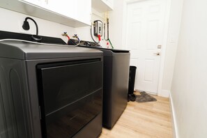 A laundry room with two stacked washing machines and a dryer, a white door, and a black trash bin.