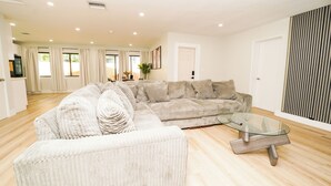 A modern living room with a sectional sofa, a glass coffee table, and a wooden floor. - Luxury 3BR Retreat - Modern Comfort in Fort Lauderdale (Fort Lauderdale)