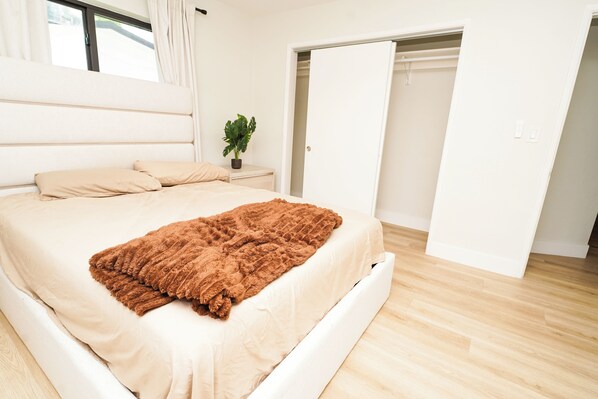 A bedroom with a bed, a nightstand, a potted plant, and a closet.