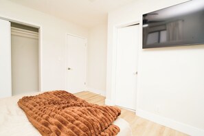 A bedroom with a bed, a TV mounted on the wall, and two doors.