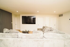 A modern living room with a large sofa, a glass coffee table, and a flat-screen TV mounted on the wall.