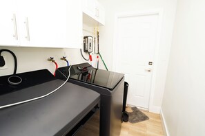 A room with a massage table, a black trash bin, a white door, and a white wall with a white cabinet.