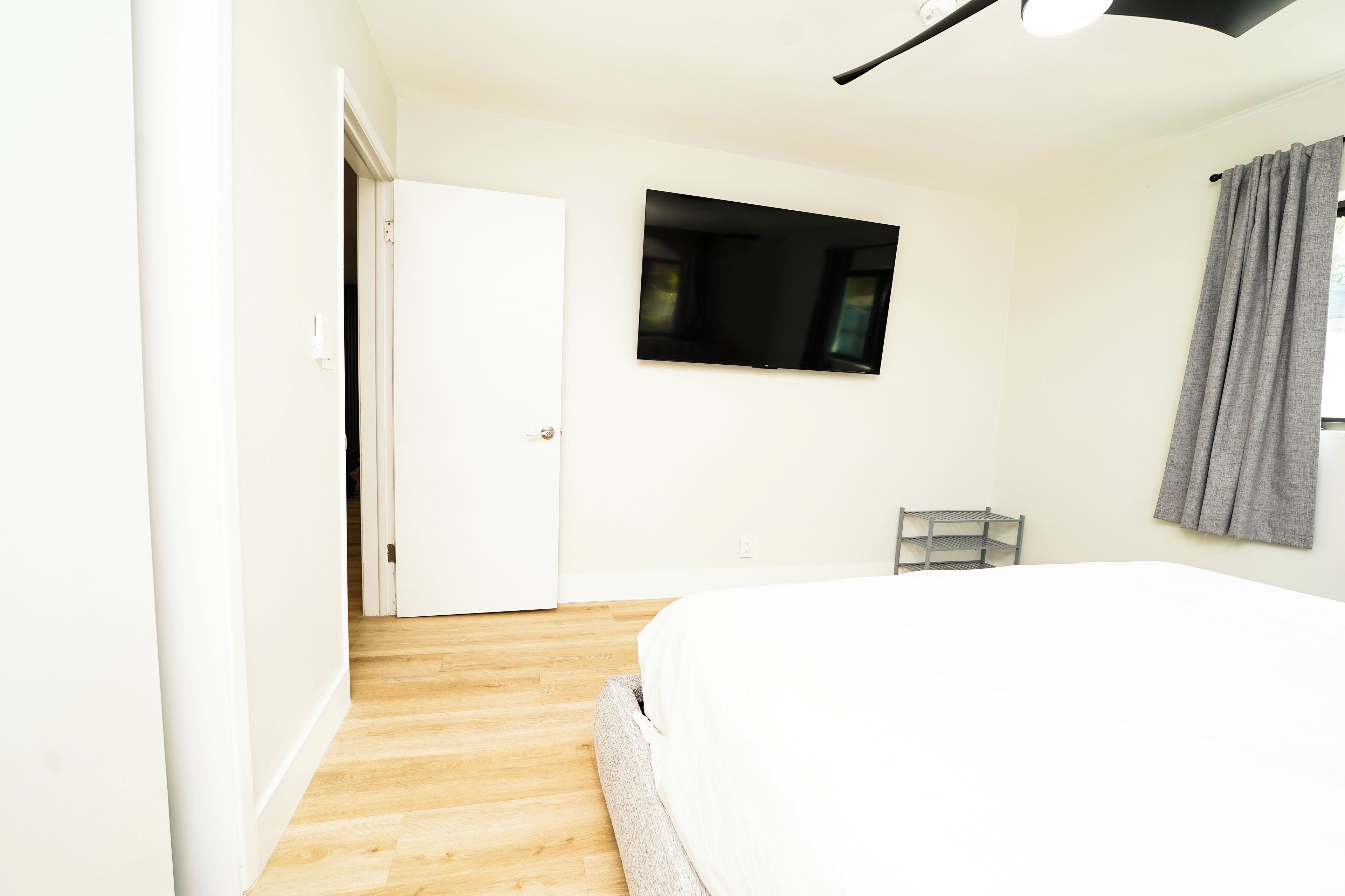 A bedroom with a bed, a television mounted on the wall, a door, and a window with curtains.