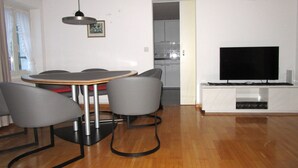 A modern living room with a dining area, a flat-screen TV, and a kitchen in the background. - Wohnung mit Sicht auf den Landsgemeindeplatz. (Appenzell)