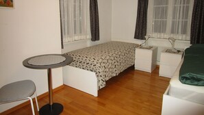 A small, tidy room with a single bed, a desk, a chair, and two windows with curtains. - Wohnung mit Sicht auf den Landsgemeindeplatz. (Appenzell)