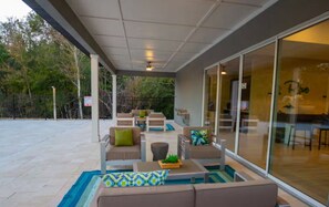 An outdoor patio with seating, a small table, and a glass door leading to an interior space. - Disney Getaway 4BD Home wITH Private Pool and BBQ (Kissimmee)