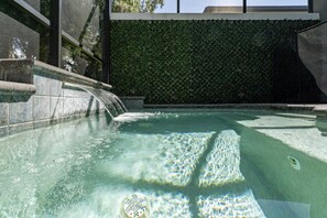 A swimming pool with a waterfall feature, surrounded by a hedge wall. - Disney Getaway 4BD Home wITH Private Pool and BBQ (Kissimmee)