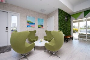 Ein modernes Interieur mit zwei grünen Sesseln um einen kleinen Tisch, einer grünen Wand mit Pflanzen und Ausblick nach außen.