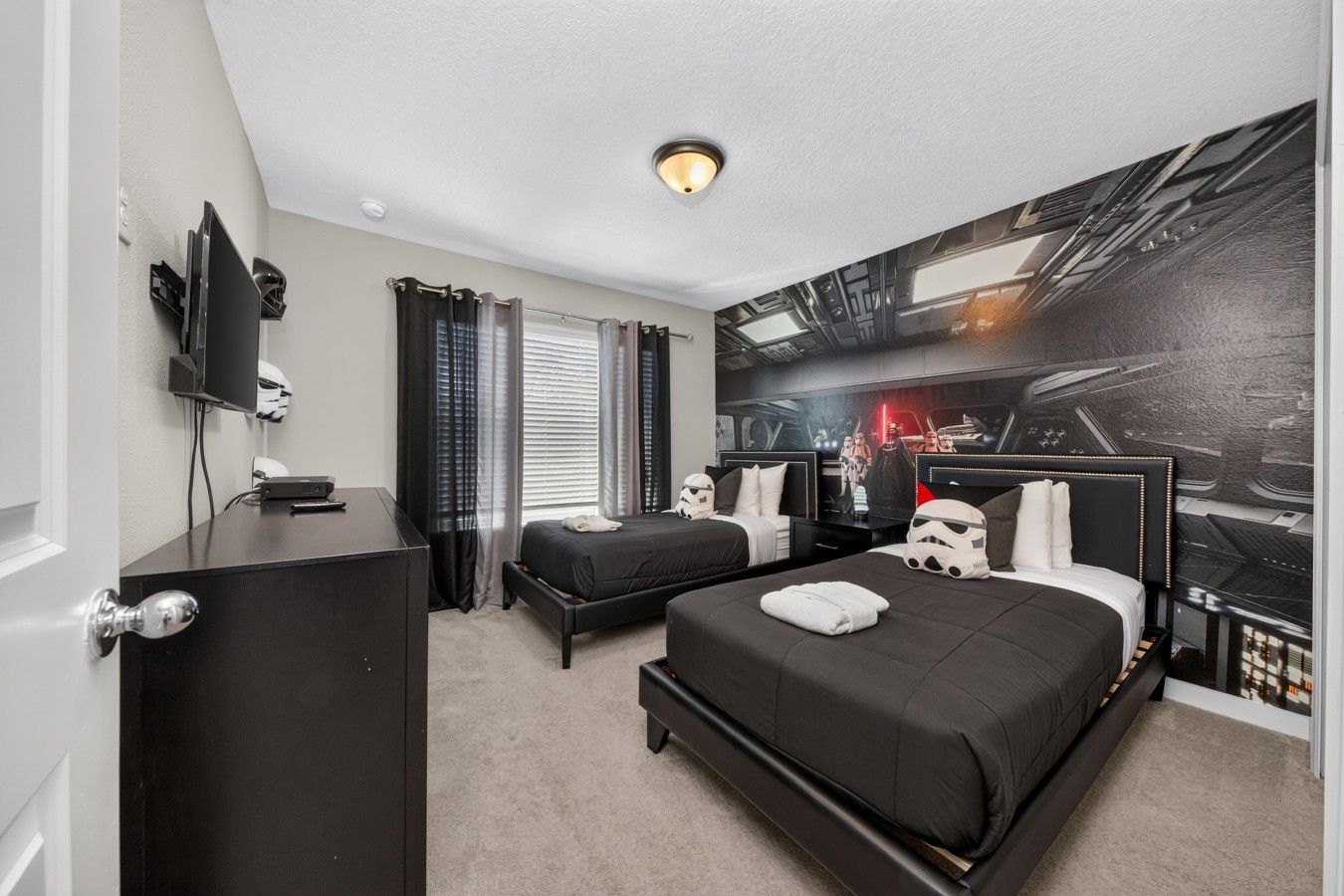 A hotel room with a large bed, a smaller bed, a desk, a television, and Star Wars-themed decor.