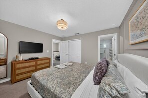 Ein Schlafzimmer mit Bett, Kommode, Fernseher und einer Tür zum Badezimmer.