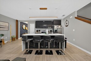A modern kitchen with a central island, bar stools, and a clock on the wall. - Disney Getaway 4BD Home wITH Private Pool and BBQ (Kissimmee)