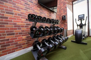 Ein Fitnessraum mit Backsteinwand, einer Reihe von Kurzhanteln und einem Ergometer.