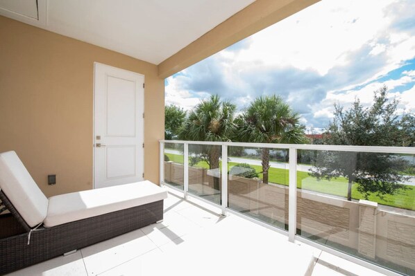 Een balkon met een witte balustrade, een witte deur en uitzicht op een groen landschap met bomen en een heldere lucht.