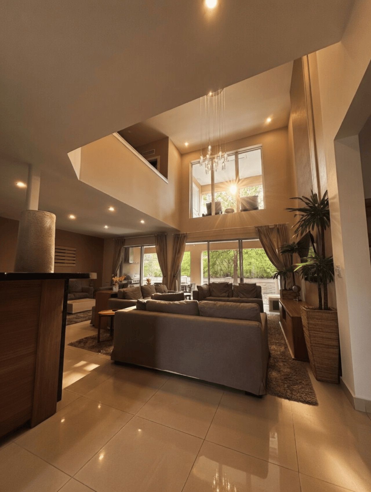 A spacious living area with a large sofa, a dining table, and a kitchen area. There is a staircase leading to an upper level.