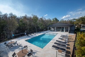 Una piscina con sillones de descanso y una zona cubierta, rodeada de árboles.