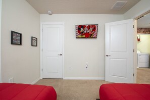 A room with two white doors, a red bed, a wall-mounted picture, and a laundry area. - 5BD Family Home with Pool BBQ and Themed Rooms (Davenport)
