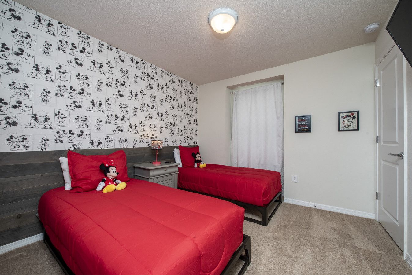 A room with two beds, a nightstand, a Mickey Mouse plush toy, and a wall with Mickey Mouse sketches.