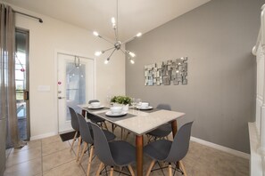 Un coin repas avec une table dressée pour quatre personnes, des chaises, un lustre moderne et un élément décoratif mural.