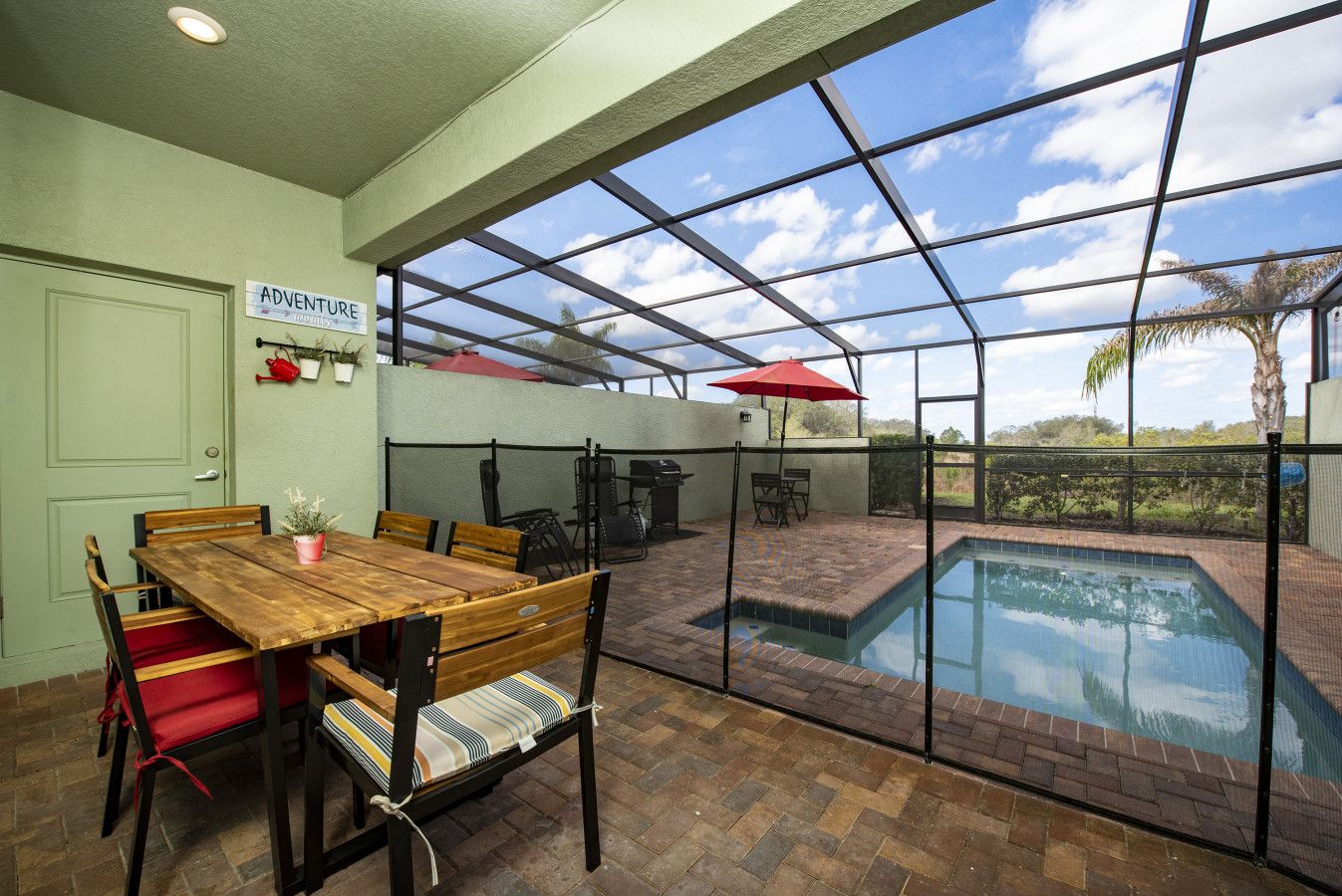 Un espace intérieur/extérieur doté d’une piscine, d’un coin repas avec une table et des chaises en bois, et d’une pancarte sur laquelle on peut lire « AVENTURE ».