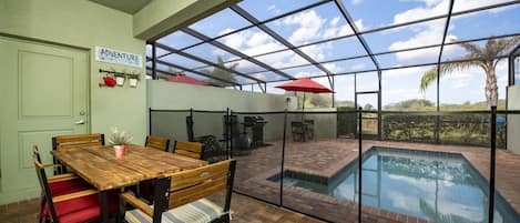 Un espace intérieur/extérieur doté d’une piscine, d’un coin repas avec une table et des chaises en bois, et d’une pancarte sur laquelle on peut lire « AVENTURE ».