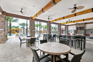 An outdoor patio area with round tables and chairs, a pool with slides, and a bar area with a television. - 5BD Family Home with Pool BBQ and Themed Rooms (Davenport)