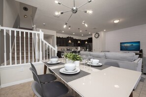 A modern kitchen with dark cabinets, a dining area with a white table and chairs, and a staircase with white railings. - 5BD Family Home with Pool BBQ and Themed Rooms (Davenport)