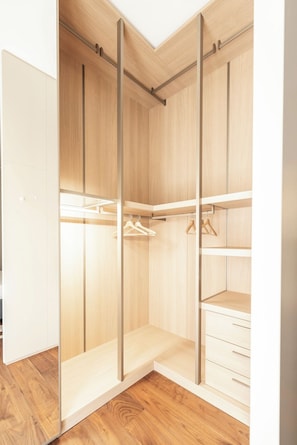 Ein begehbarer Kleiderschrank mit Holztüren, einer Kleiderstange und Regale.