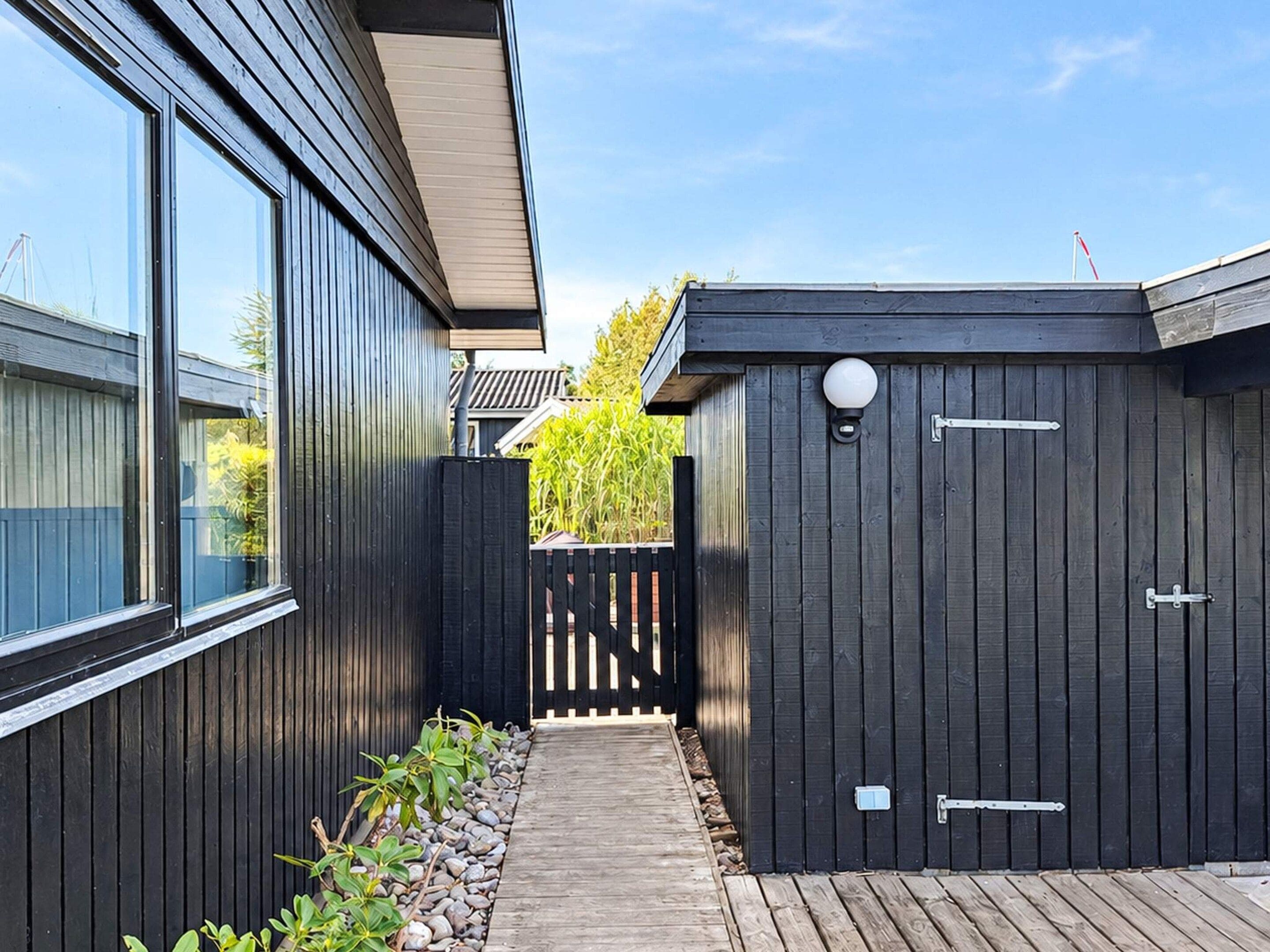 A wooden deck leading to a dark wooden shed with a white light fixture and a metal latch.