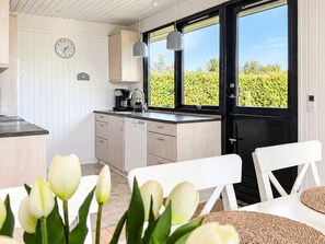 A modern kitchen with a clock, a coffee maker, and a window with a view of greenery. - 6 Person Holiday Home in Juelsminde (Juelsminde)